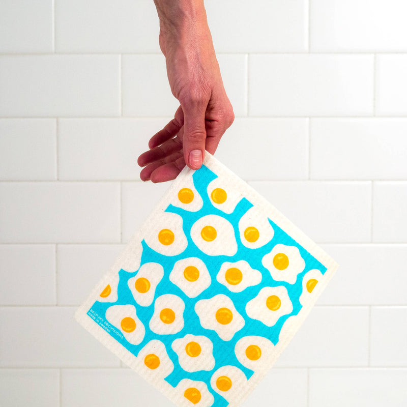 Bespoke Provisions - Eggs Swedish Dishcloth held over a napkin, showcasing its design and highlighting its utility for cleaning tasks.