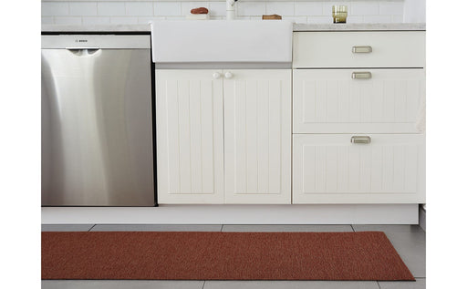 White kitchen setup featuring a white cabinet with silver handles, showcasing the Chilewich | Martha Stewart Heathered Shag - Burnt Coral rug on a tile floor.