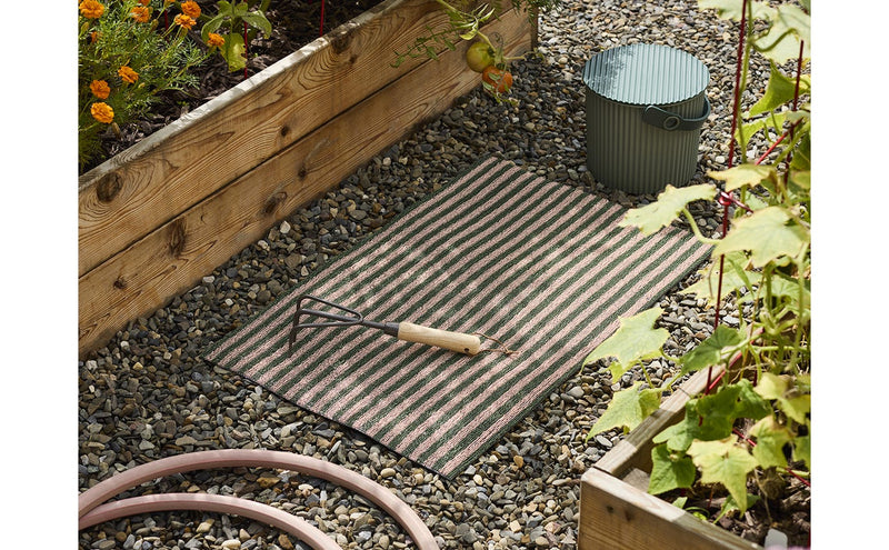 Chilewich | Breton Stripe Shag Mat - Malibu, a durable rug with tufted texture, suitable for outdoor use, displayed with garden tools on gravel.