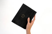 Hand holding a black leather L'ATELIER DU VIN notebook, embodying the Nomad Collection's elegance, perfect for gifting or special occasions.
