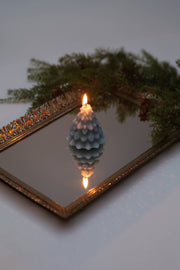 Mo&Co Home Exclusive: Sculpted Beeswax Tree Candle on a gold-trimmed mirror, reflecting its flame. Handcrafted, inspired by vintage ornaments; perfect for elegant holiday decor.