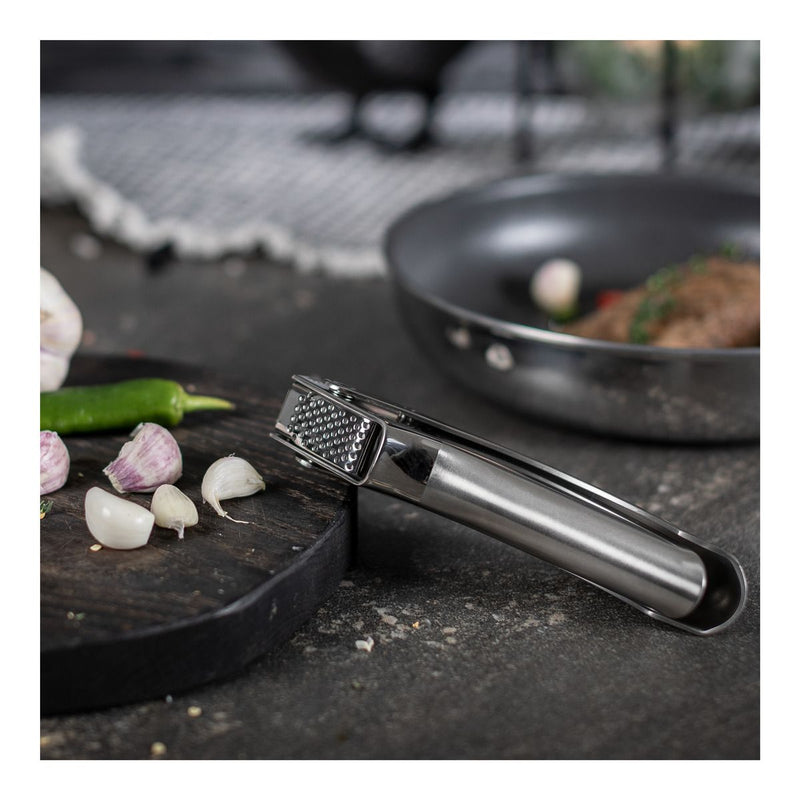 Kuhn Rikon | Epicurean Garlic Press on countertop beside garlic and chili, emphasizing ergonomic design and easy-clean sieve for optimal flavor extraction.
