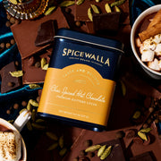 Spicewalla | Chai Spiced Hot Chocolate tin surrounded by chocolate squares, whole spices, and two mugs of hot chocolate with marshmallows and cinnamon sticks.