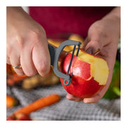 Close-up of hands using Kuhn Rikon | Original Swiss Peeler - Grey to peel a red apple, showcasing its razor-sharp carbon steel blades and ergonomic design.