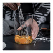 Close-up of Kuhn Rikon | ESSENTIAL Ball Whisk being used to beat eggs in a glass container, showcasing its innovative design for effective mixing.