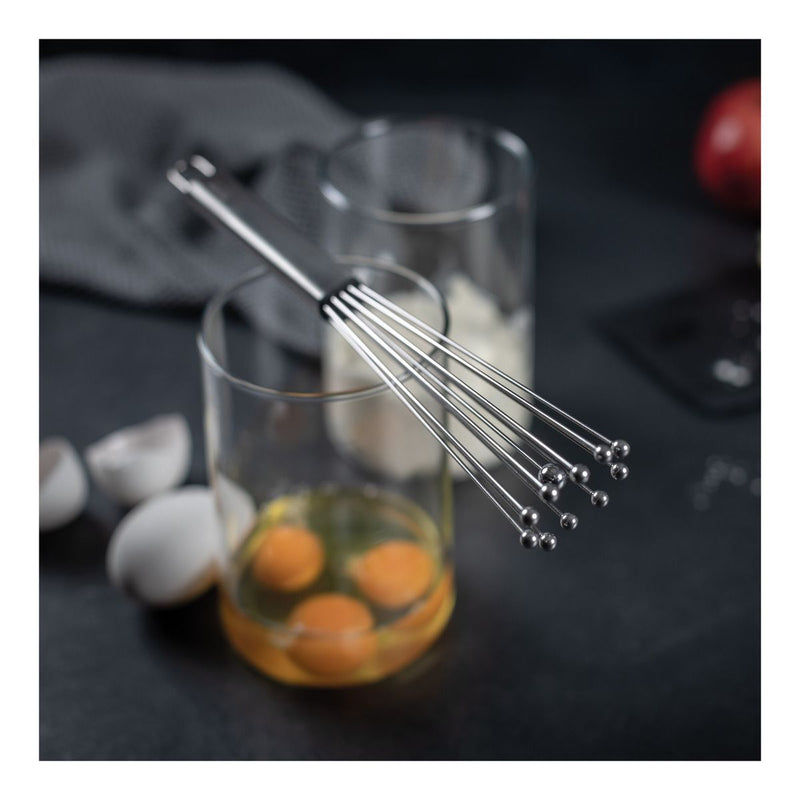 Kuhn Rikon | ESSENTIAL Ball Whisk rests on a glass of cracked eggs, showcasing its innovative design for efficient mixing and easy cleaning.