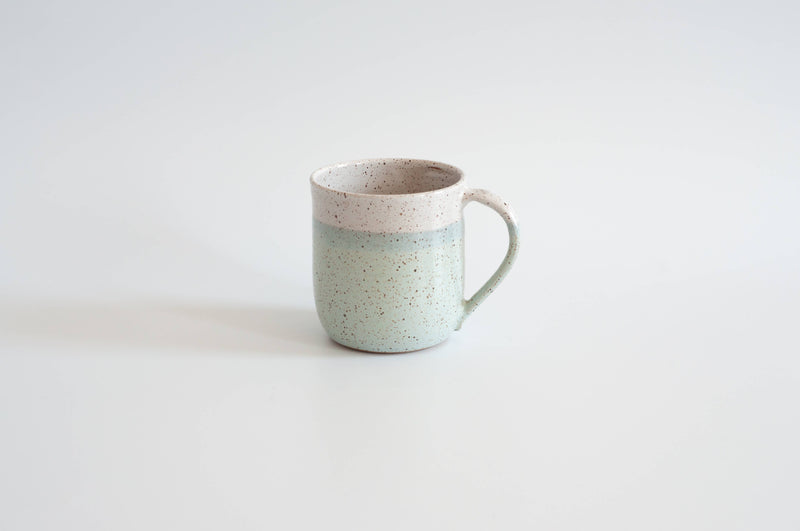 RachaelPots - 12 Oz Original Mug: Sage, a handmade ceramic mug with a mint-green speckled glaze and beige band, featuring a thumb rest handle. Perfect for coffee or tea.