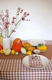 Linen tablecloth in Cinnamon gingham on table with vase, vegetables, and tableware, showcasing rustic dining style and durability.