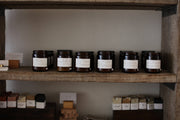 Among the Flowers - Essential Oil + Soy Wax Candle: Sitka, displayed on a shelf amidst various jars, featuring chamomile, bergamot, sage, and cedar scents.