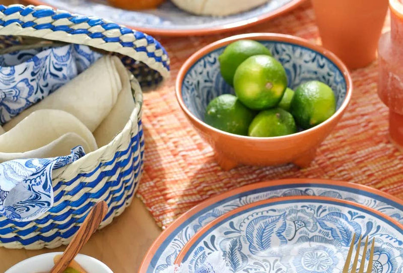 Verve Culture - Mexican Woven Palm Tortilla Basket showcased on a tabletop with a footed bowl of limes, a plate, and a gold-tone fork.