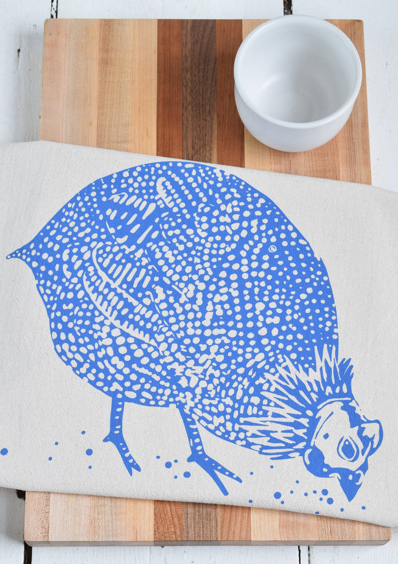 Hearth and Harrow - Organic Cotton Guinea Hen Tea Towel featuring a blue-violet hen design; showcased on a wooden surface beside ceramic kitchenware.
