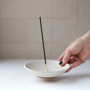 Hand holding a Gravesco Pottery incense burner with a black incense stick, showcasing its function to catch ash; ideal for enhancing home ambiance.