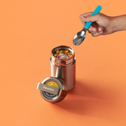 PlanetBox Insulated Container on orange surface, open with chunky soup, spoon poised above. Stainless steel, vacuum-sealed for temperature retention, featuring leakproof lid.