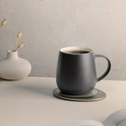 OHOM - Ui 3 Self-heating Mug Set: Jasmine White, on a warmer, with a vase and open book nearby, exemplifying elegance and convenience.