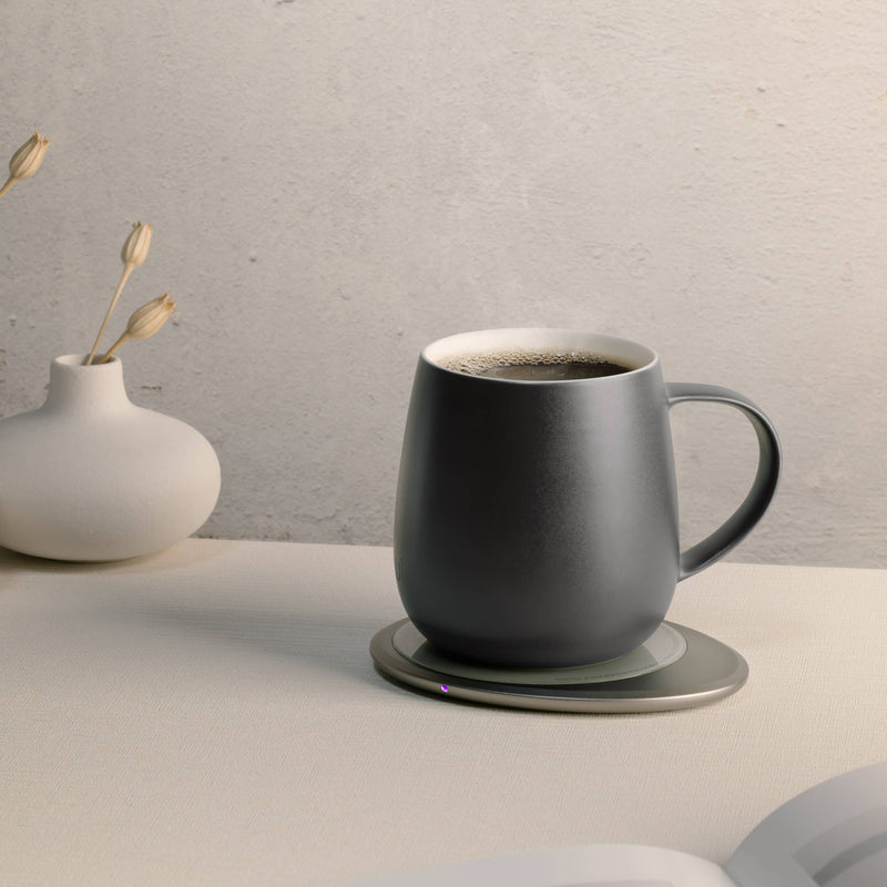OHOM - Ui 3 Self-heating Mug Set: Jasmine White, on a warmer, with a vase and open book nearby, exemplifying elegance and convenience.