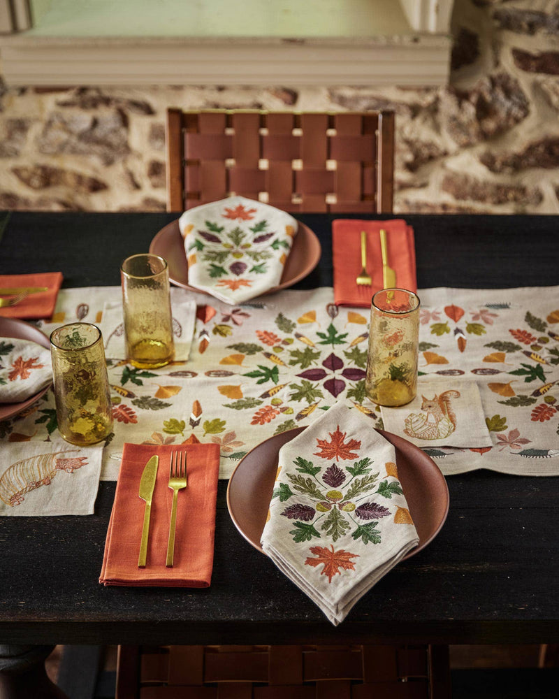 Coral & Tusk - Pressed Leaves Dinner Napkin, elegantly embroidered with fall motifs and quail feathers, complements a rustic autumn table setting at Athens Cooks.