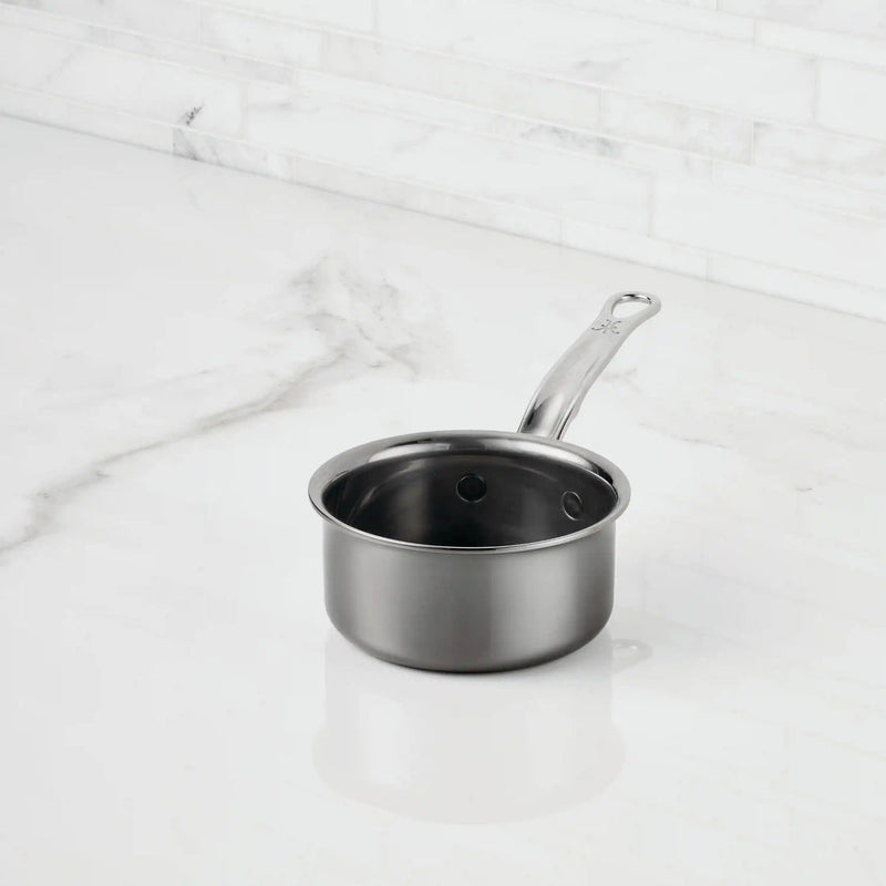 Hestan | Cookware, .75qt Butter Warmer Pan, a stainless-steel saucepan with a long handle, on a marble countertop, ideal for precise melting and cooking.