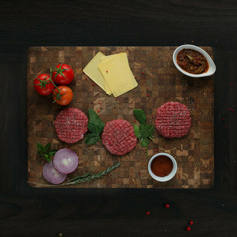 Teakhaus Butcher Block Rectangle Cutting Board on a wooden surface, with tomatoes and brown powder nearby, showcasing its durable, eco-friendly design and smooth texture for kitchen use.