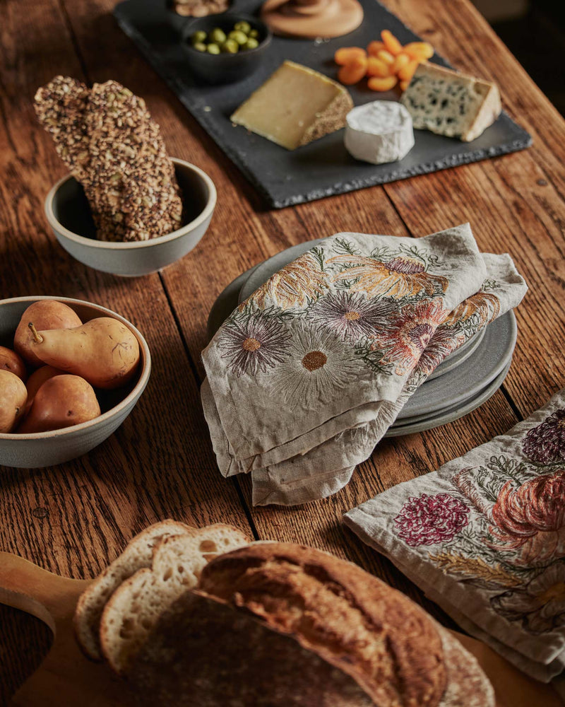 Coral & Tusk - Autumn Blossoms Dinner Napkin on a cozy cheese-and-bread setup with artisanal breads, cheeses, crackers, and ripe pears, styled with rustic ceramics.