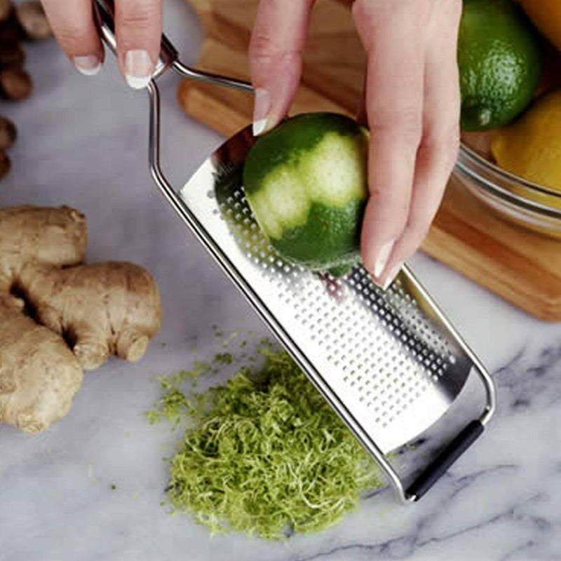 Microplane Professional Series Grater zesting a lime with ginger root and citrus in view; features sharp stainless blades and non-slip base for efficient grating.