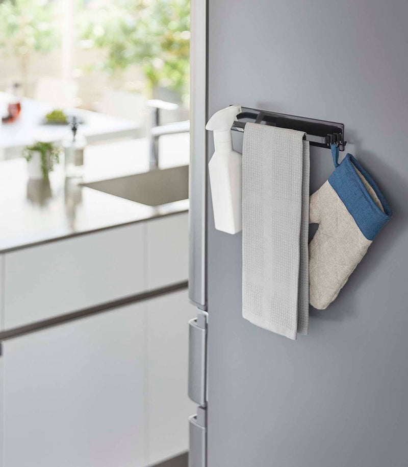 Yamazaki Home - Magnetic Kitchen Towel Hanger on fridge, holding a spray bottle, kitchen towel, and oven mitt, showcasing its organizing capability in a modern kitchen setting.