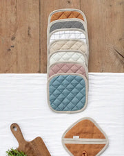 MagicLinen linen pot-holder in charcoal gray, featuring quilted detailing and a convenient hanging loop, displayed alongside kitchen accessories on a wooden surface.