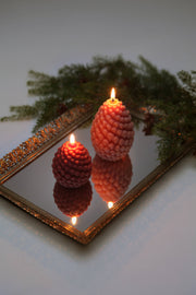 Mo&Co Home Exclusive: Sculpted Beeswax Pine Cone Candles on a mirrored surface, featuring hand-poured beeswax design, evoking holiday nostalgia in elegant, contemporary style. Available in two sizes.