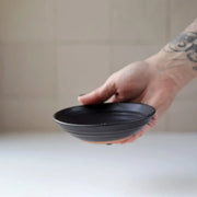 Hand holding Gravesco Pottery Incense Burner, a black ceramic dish for incense sticks, showcasing handcrafted design with visible unglazed clay edge. Ideal for catching ash.