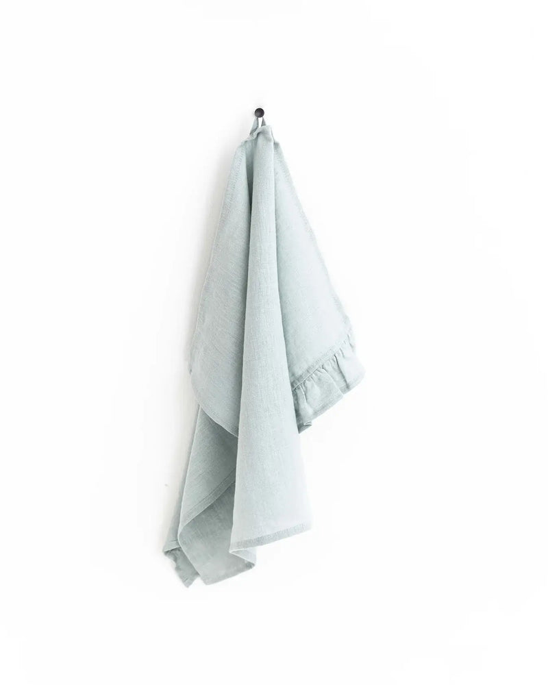 MagicLinen Ruffle Trim Tea Towel hanging on a hook, showcasing its soft, durable linen texture and practical loop for easy kitchen use.