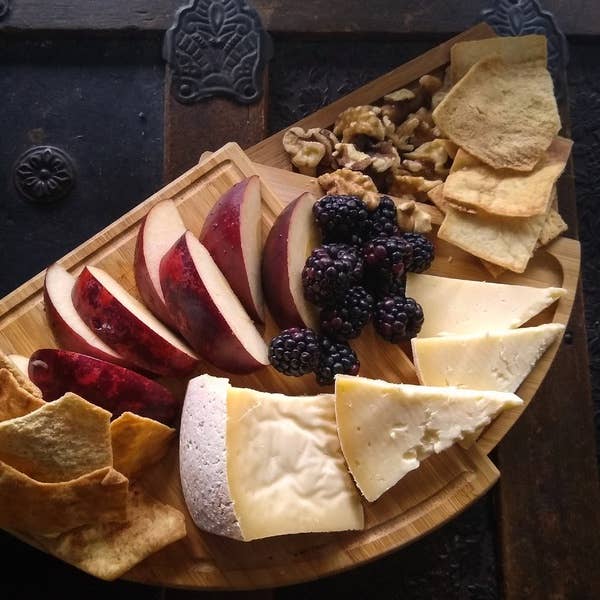 Tulip Tree Creamery - Hops: 5 Oz. Wedge on a wooden surface, accompanied by assorted fruits and nuts, highlighting its pairing versatility with wine or beer.