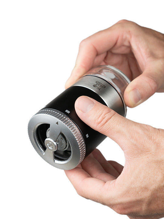 Peugeot Maestro Pepper Bar grinder with adjustable grind size, held by two hands, part of a gift set with jars and premium peppers.