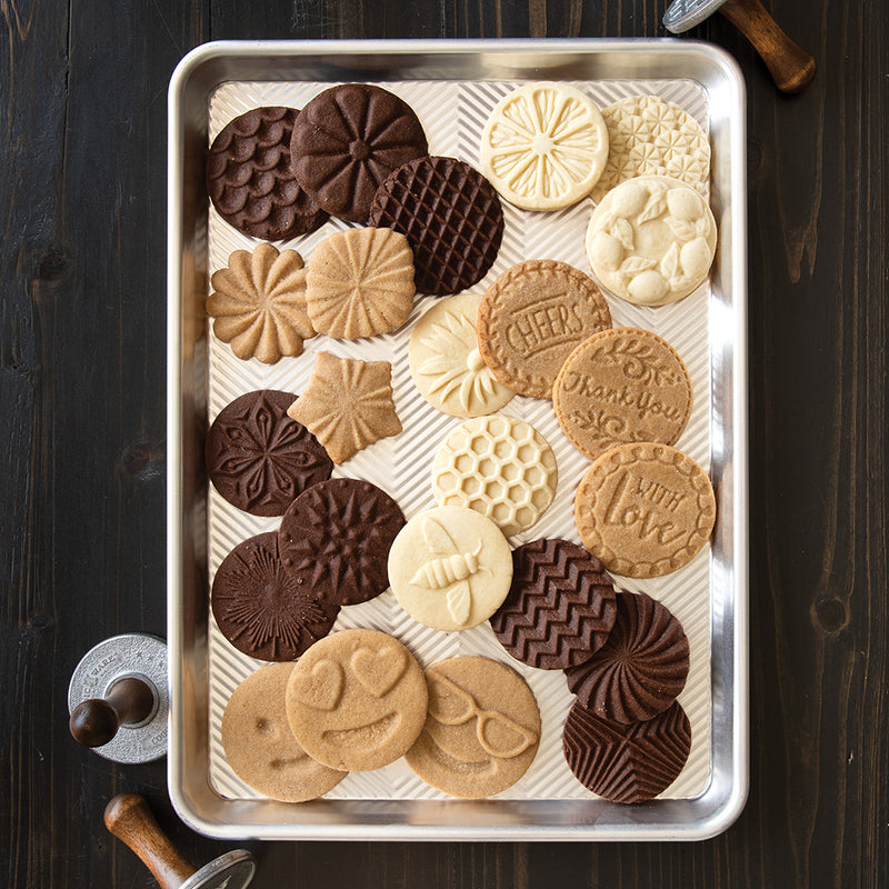 Nordic Ware | Heirloom Cookie Stamps displayed on a tray with cookies featuring intricate bee and flower designs, showcasing detailed patterns for baking enthusiasts.