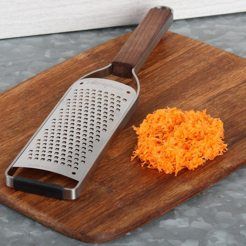 Microplane | Master Series Coarse Grater with Walnut Handle on cutting board, next to grated carrots, highlighting elegant design and functionality for diverse kitchen tasks.