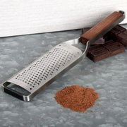 Microplane | Master Series Coarse Grater with Walnut Handle beside chocolate squares and finely grated chocolate on a metal surface.