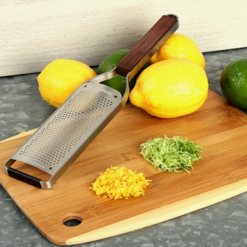 Microplane | Master Series Fine Grater with Walnut Handle on a cutting board with lemon and lime zest, alongside whole lemons and a lime.