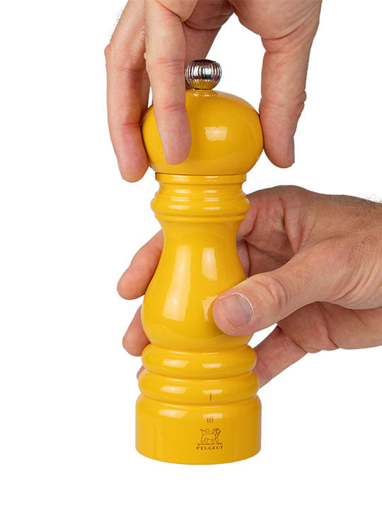 Peugeot Paris U'Select Saffron Salt Mill, 7 inches, being adjusted by hand, featuring a metal knob and Peugeot logo, known for its ergonomic design and precise grinding.