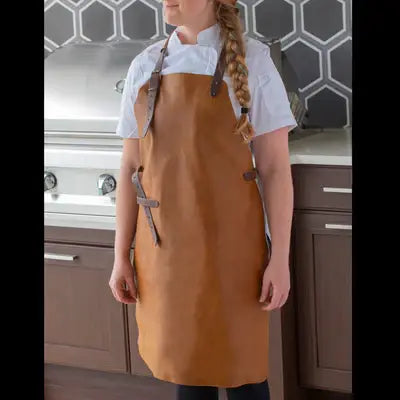 Person wearing Messermeister - Vintage Leather Apron - Amber in kitchen, featuring adjustable leather straps and towel holder, showcasing high-quality craftsmanship with a timeless design.