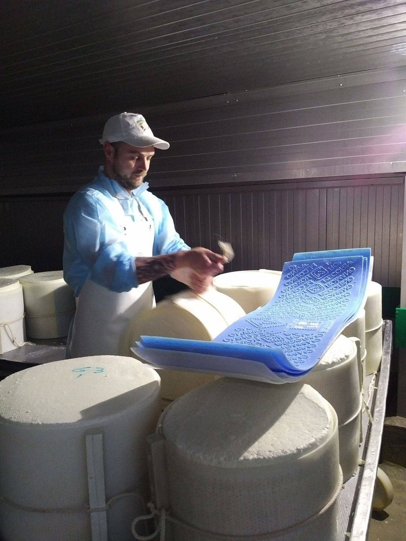 Nicola's Marketplace - Genuine Fulvi® Pecorino Romano DOP: 7 Ounces, showcased in a cheese-making room with a man handling fresh cheese wheels, emphasizing its artisanal origin.