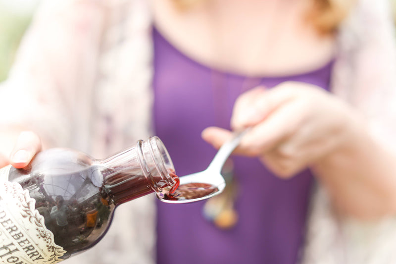 Roots And Leaves - Elderberry & Honey Tonic, 16 oz, being poured into a spoon, highlighting its herbal blend for immune support. Perfect for enhancing kitchen remedies.