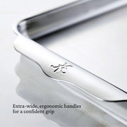 Close-up of Hestan | Oven Bond Tri-Ply Bakeware, Quarter Sheet Pan, showcasing its wide ergonomic stainless-steel handle with brand emblem, designed for confident grip and even heat distribution.