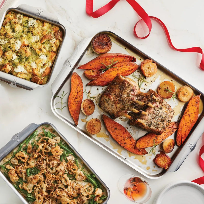Festive meal featuring Hestan | Oven Bond Tri-Ply 5 Piece Set with roasted lamb, sweet potatoes, caramelized onions, green-bean casserole, and bread stuffing, showcasing elegant ovenware performance.