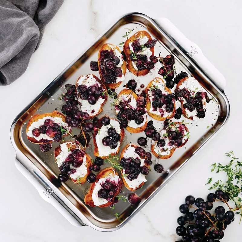 Hestan Provisions OvenBond Medium Sheet Pan showcasing crostini with cheese, grapes, and thyme, highlighting its even heat distribution and durable stainless-steel craftsmanship.