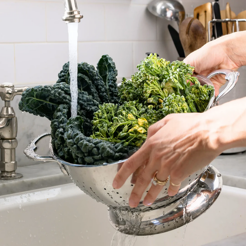 Hestan Provisions | Stainless Steel Colanders, 5 Quart, used for rinsing kale and broccoli under running tap, showcasing superior drainage and durability.