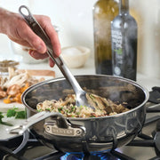 Person using a Stainless Steel Deep Spoon, 13 to stir food in a pot on the stove, showcasing practical kitchenware from Athens Cooks.