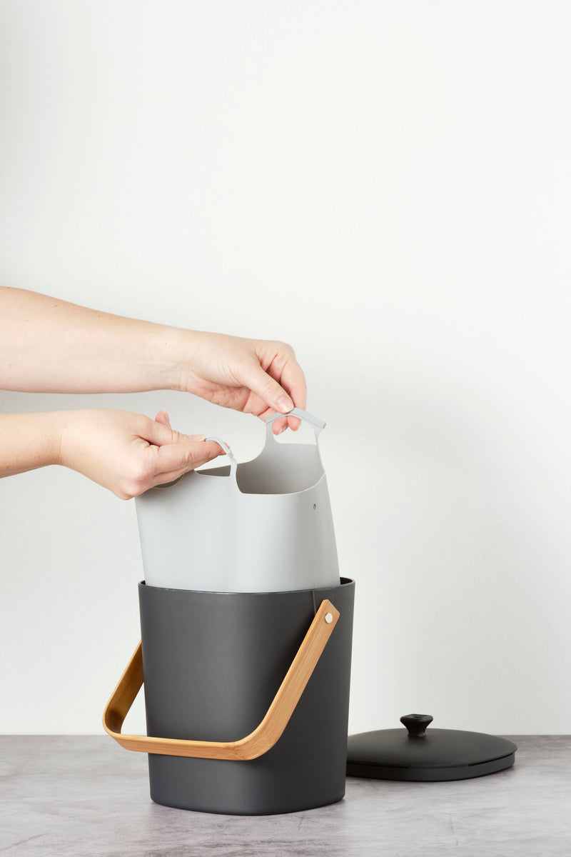 Hands holding Bamboozle - Composter Reusable Liner with grip loop, designed for easy compost transfer; durable silicone construction for practicality and style.