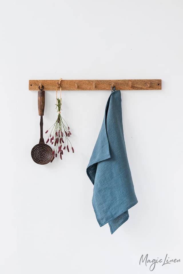 Linen tea towel displayed on a wooden rack with utensils, featuring a blue towel hanging by a loop, ideal for maintaining kitchen cleanliness.