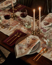 Coral & Tusk - Autumn Blossoms Dinner Napkin elegantly folded on gray-green plates, complements a cozy, fall-inspired table setting with brass accents and lit candles.