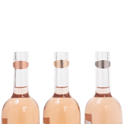 L'Atelier du Vin - USA - Drop Stopper - LE TRIO WINE RINGS on clear bottles, featuring pink, silver, and gold matte memory metal with absorbent felt.