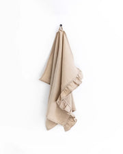Ruffle trim linen tea towel hanging on a hook, showcasing its soft texture and practical loop for easy kitchen use.