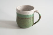 RachaelPots - 12 Oz Original Mug: Sage, crafted from speckled stoneware, features a green and off-white glaze with a thumb rest on the handle.